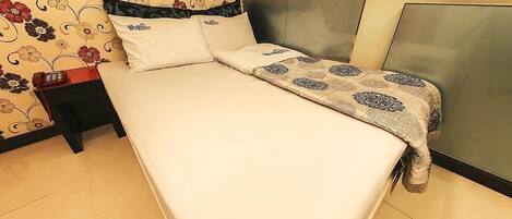 A neatly made bed with a patterned bedspread, a bedside table with a phone, and a floral wallpaper.