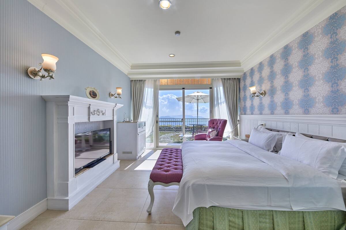 Une chambre d’hôtel avec un grand lit, une télévision, une cheminée, un balcon avec vue et un fauteuil.