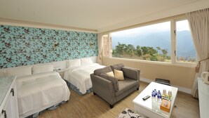 Habitación de hotel con dos camas, un sofá, una mesita con botellas de agua y vistas a montañas a través de la ventana.
