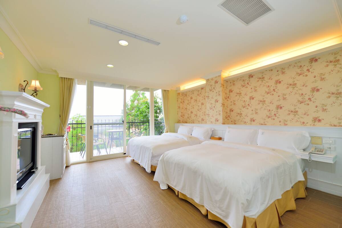 Une chambre d’hôtel avec deux lits, une télévision, une petite table et un balcon donnant sur un paysage verdoyant.
