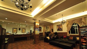 Un vestíbulo de hotel con mostrador de recepción, zona de estar y un gran ventanal con cortinas.
