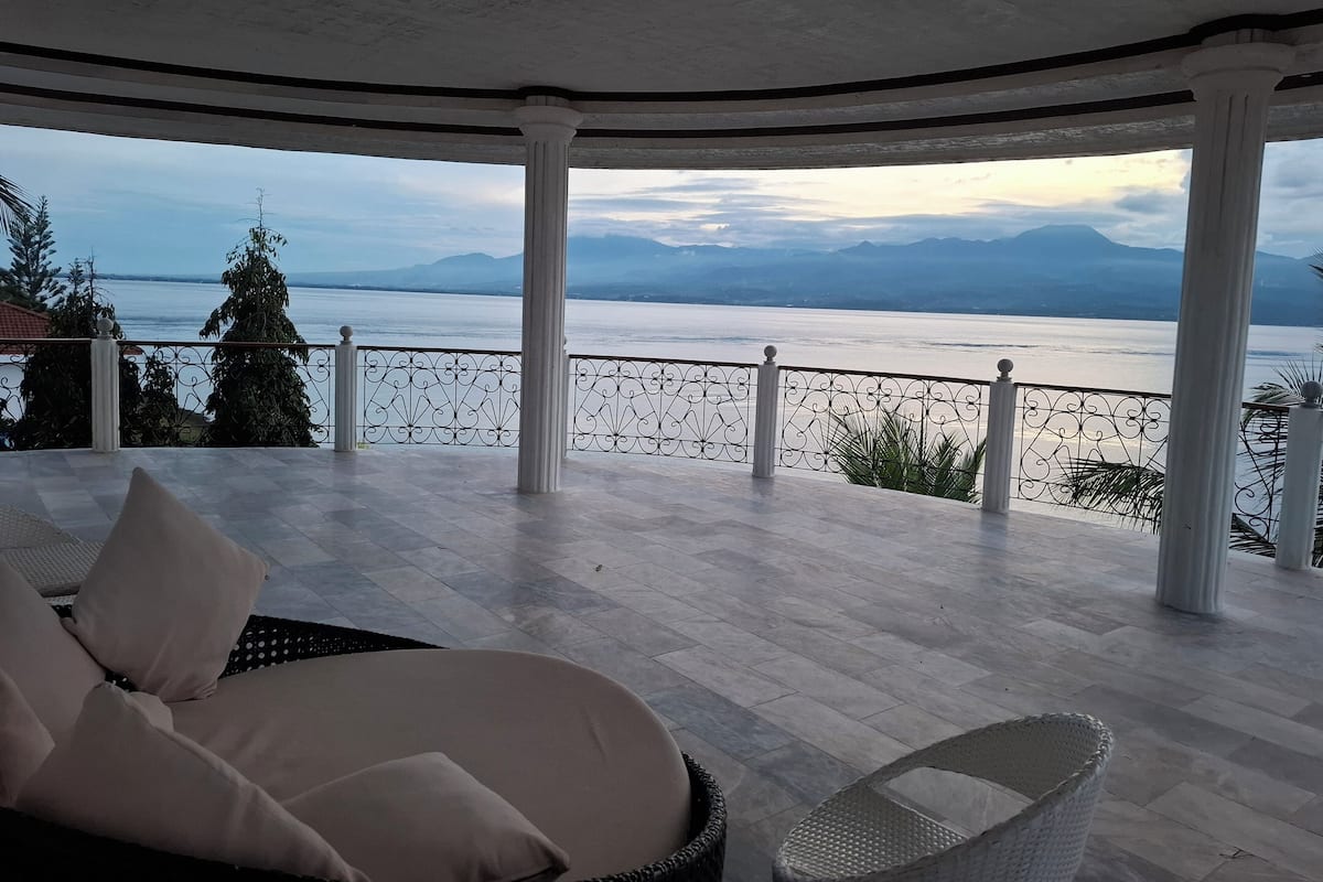 A covered outdoor seating area with a view of a lake and mountains.