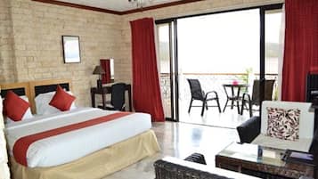 Camera d'albergo con un grande letto, un balcone con tavolo e sedie e vista sul mare.