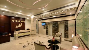 A hotel lobby with a reception desk, a TV screen, a lounge area with a sofa and armchairs, and a decorative wall with a glass display. - Lords Inn Jodhpur (Jodhpur)