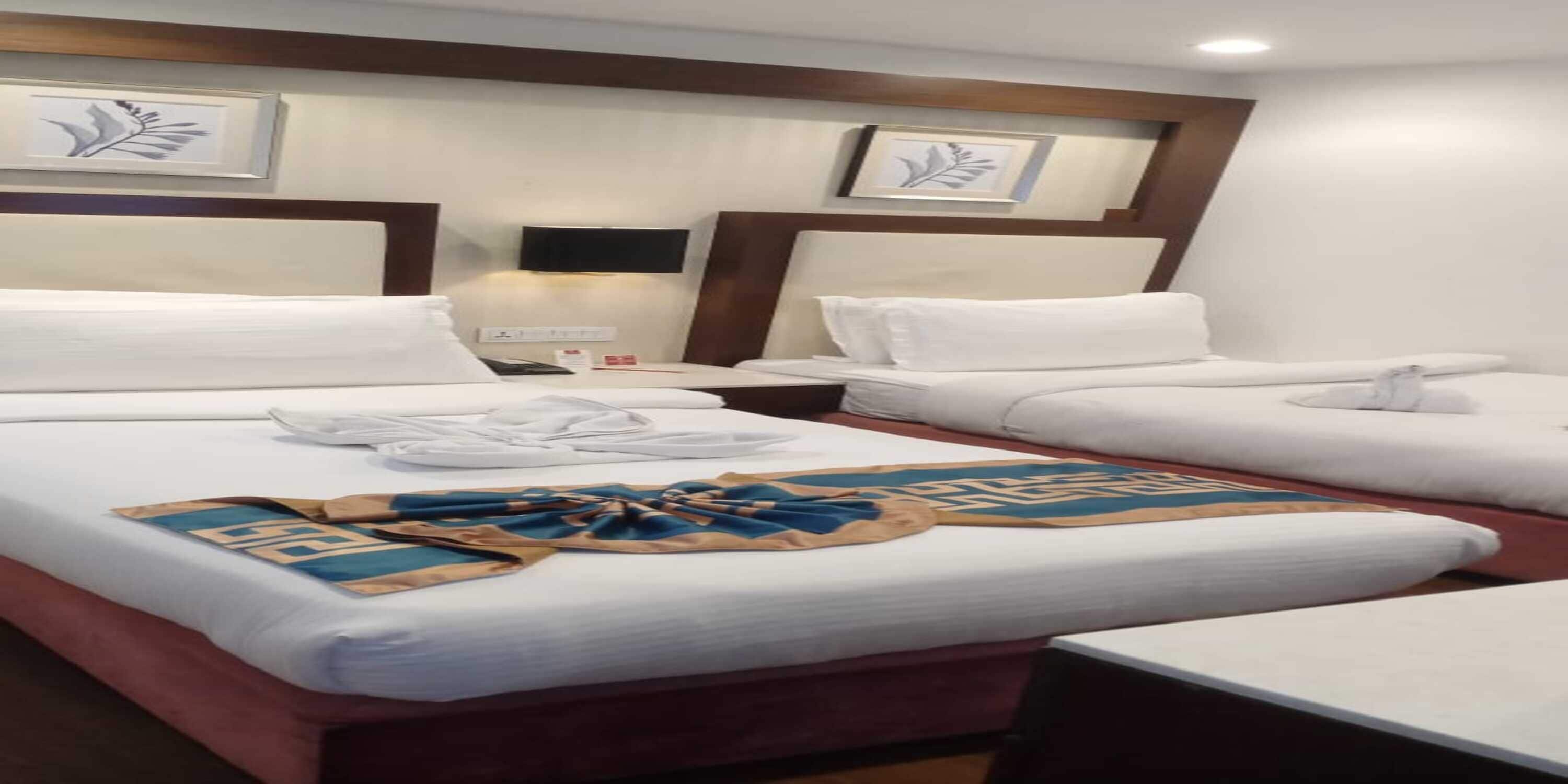 A hotel room with two beds, each with white linens and pillows. There are framed artworks on the walls above the beds.