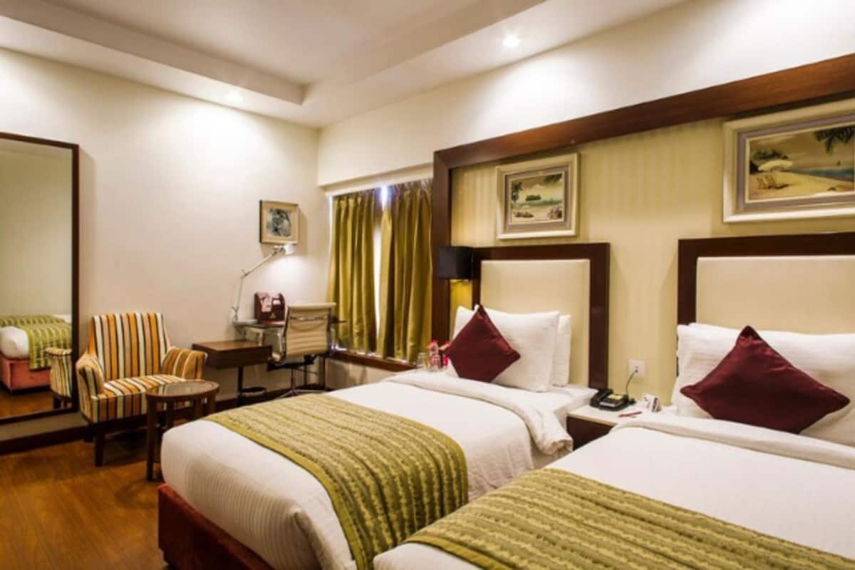 A hotel room with two beds, a desk, a chair, and a mirror.