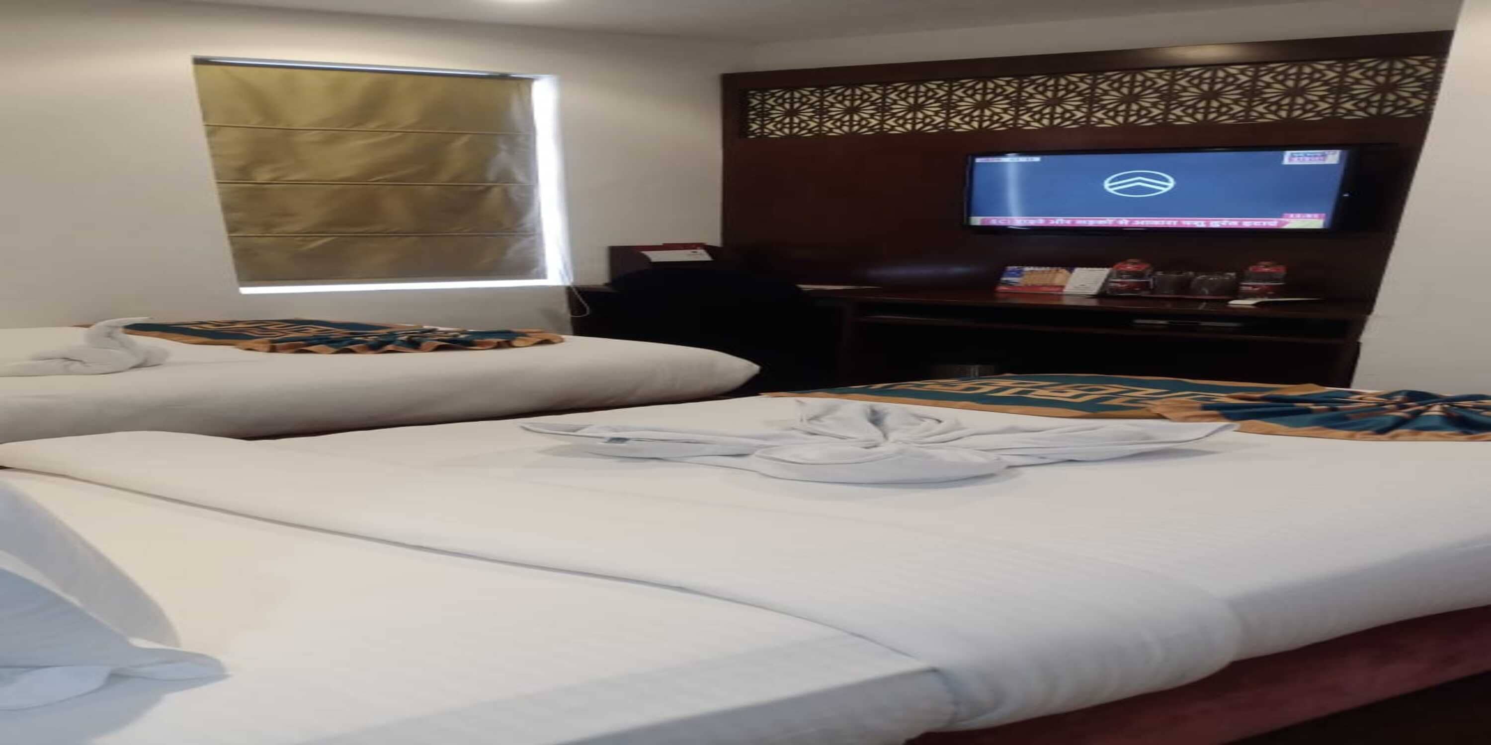 A hotel room with two beds, a television on the wall, and a window with blinds.