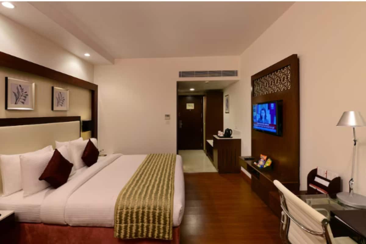 A hotel room with a bed, a desk, a TV, and a reception area.