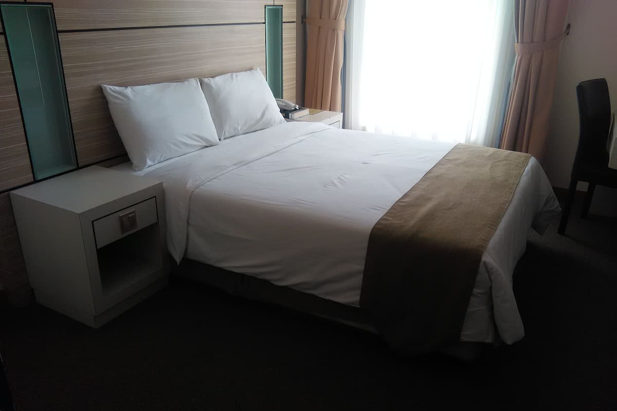 A hotel room with a bed, a nightstand, a bedside table, a chair, and a window with curtains.