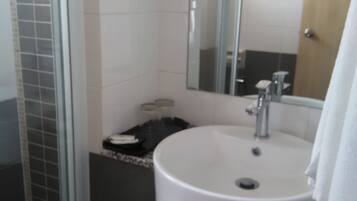 A bathroom with a white sink, a mirror, and a shower area.