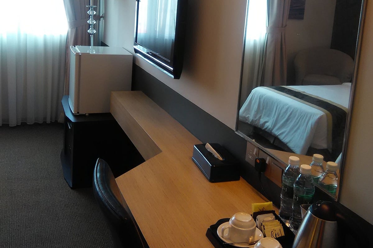 A hotel room with a bed, a desk with a computer, a TV, a lamp, and a coffee maker.