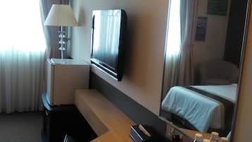 Habitación de hotel con cama, escritorio con computadora, televisor, lámpara y cafetera.