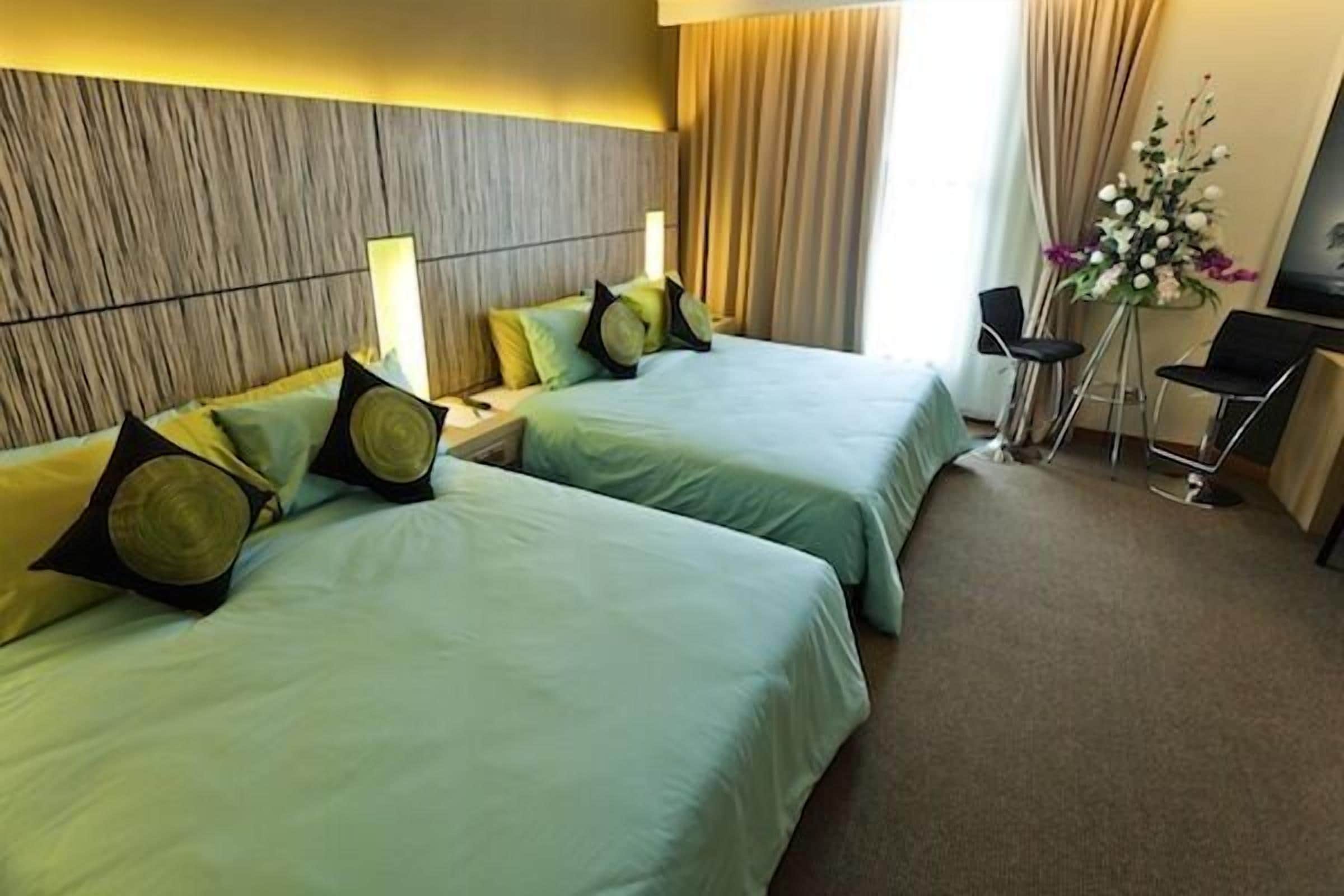 A hotel room with two beds, a desk, a chair, and a vase of flowers.