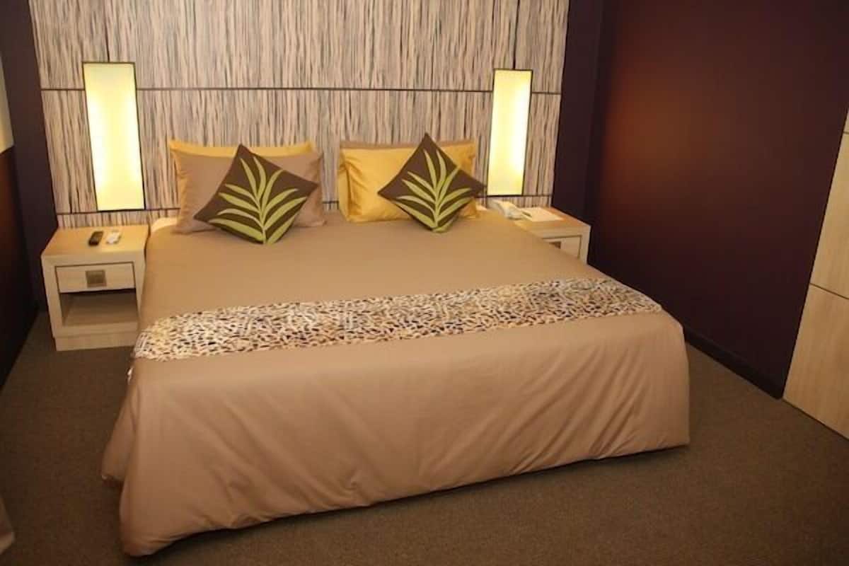 A neatly made bed with a beige bedspread and decorative pillows, flanked by bedside tables with lamps and a telephone.