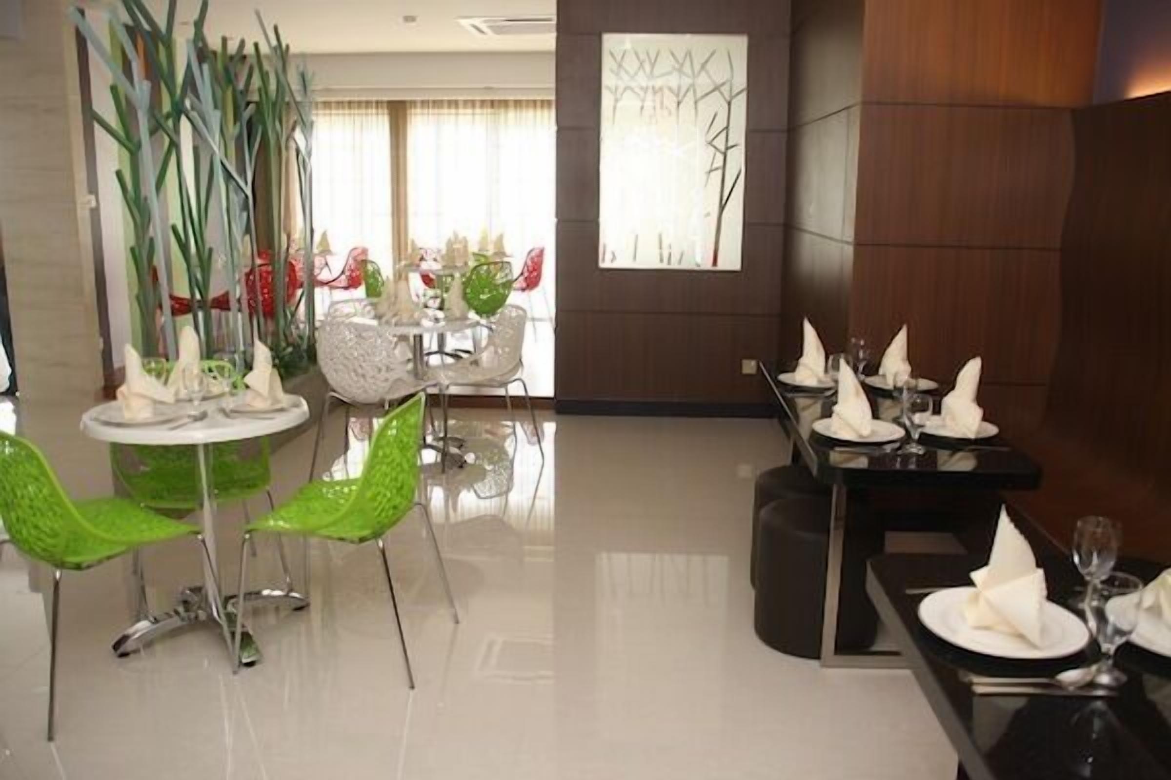 A dining area with modern furniture, including green chairs and a round table with white plates and napkins.