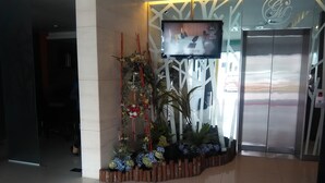 A reception area with a television displaying a room, a reception desk, and an elevator. - Grand Medallion Hotel (Kuching)