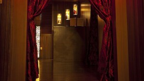 A hallway with red curtains, a wooden floor, and a staircase leading to a room with a light fixture and a framed picture. - Grand Medallion Hotel (Kuching)