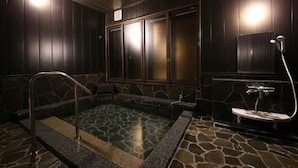 A spa room with a stone-tiled hot tub, wooden panel walls, and a glass-enclosed window.