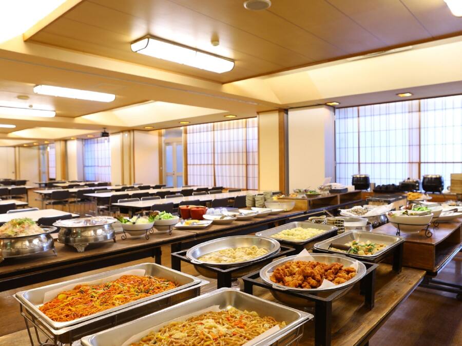 Disposição de buffet com diversos pontos de comida e mesas.