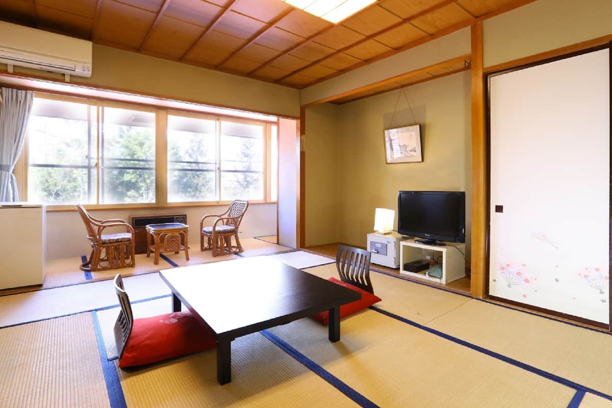 A traditional Japanese room with tatami flooring, a low table, chairs, a television, and a sliding door.
