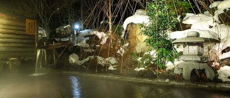 A traditional Japanese onsen with a wooden bathhouse and a stone pathway leading to a hot spring.