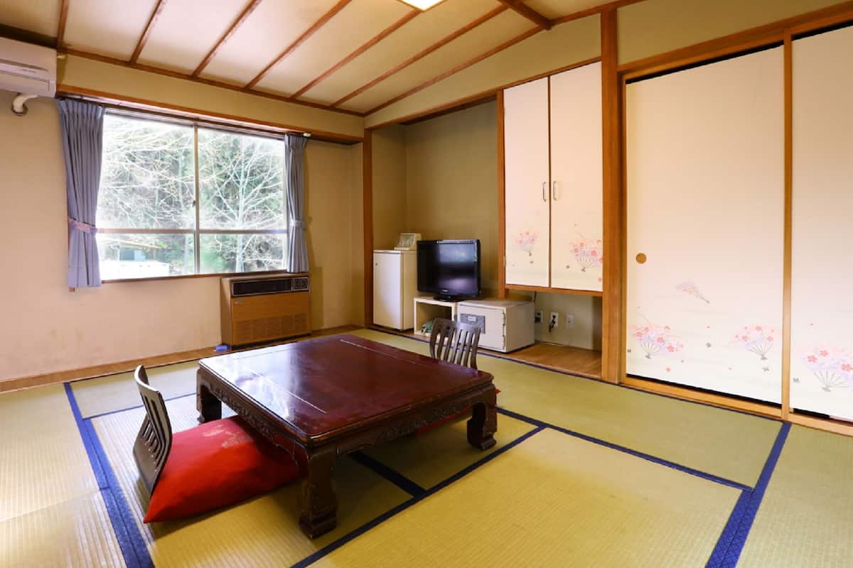 A traditional Japanese room with tatami flooring, a low table, a television, and sliding doors.