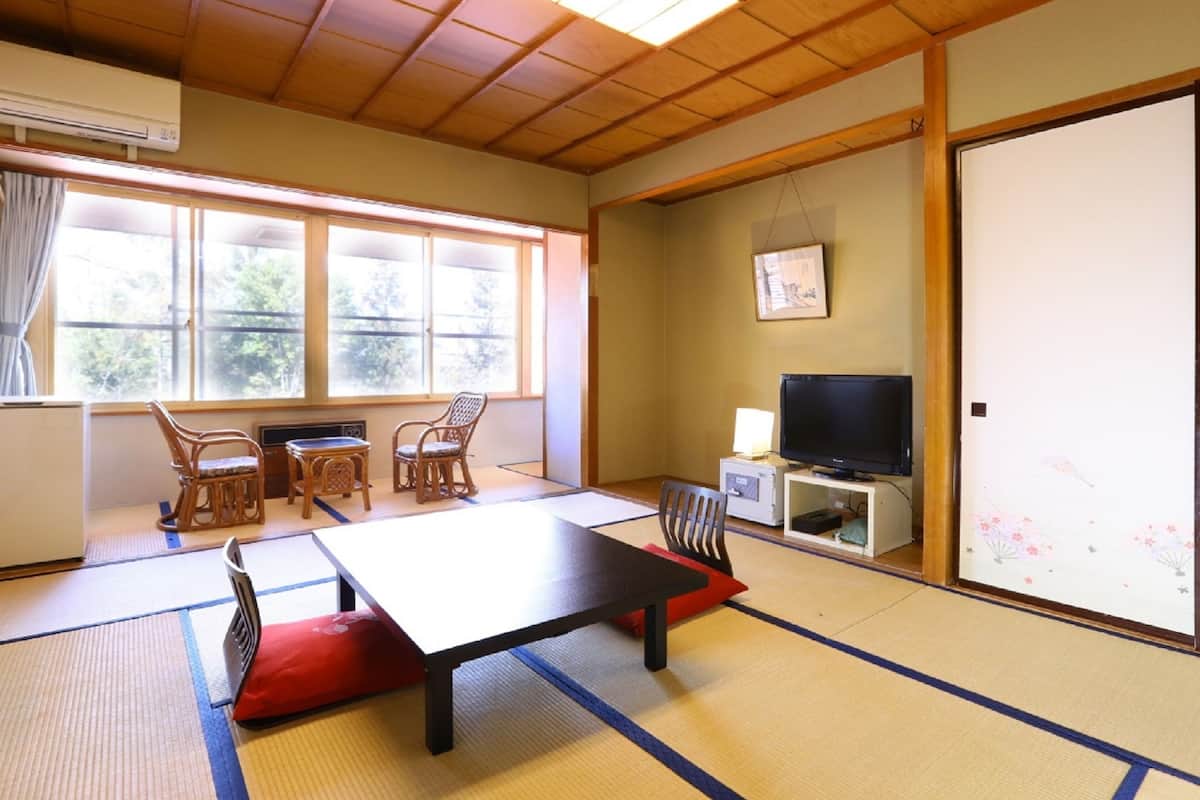 A traditional Japanese room with tatami flooring, a low table, chairs, a television, and a sliding door.