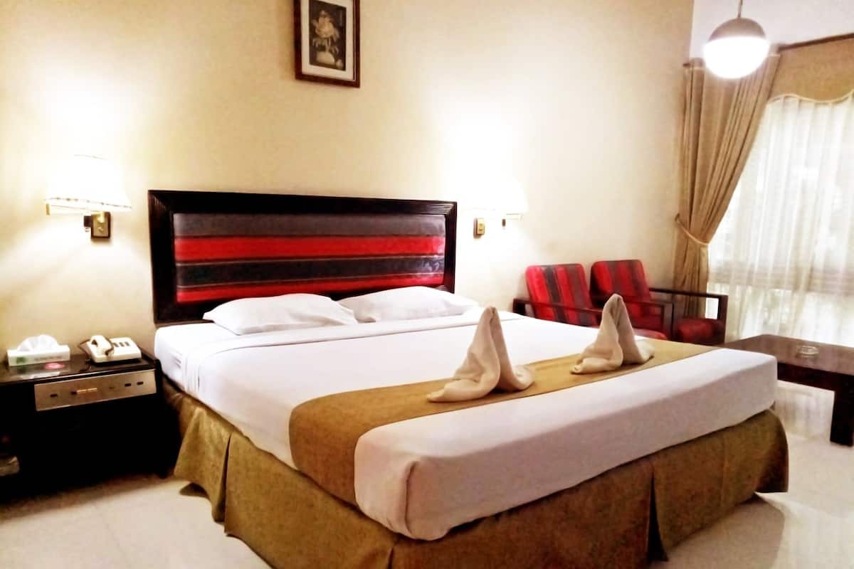 Een hotelkamer met een groot bed, een nachtkastje met een lamp, een stoel en een raam met gordijnen.