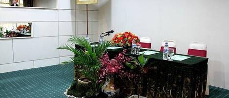 A conference room with a table set for a meeting, surrounded by potted plants and a portrait on the wall.