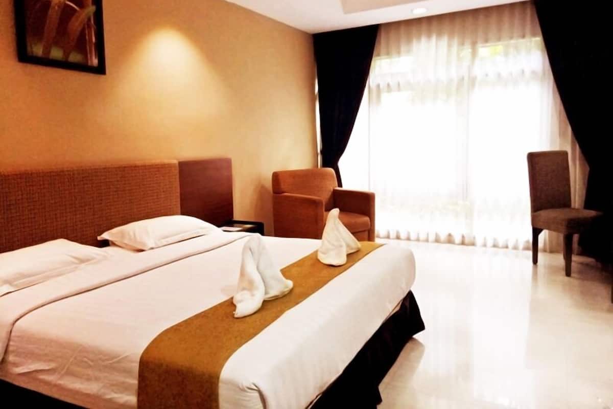 Een hotelkamer met een groot bed, twee stoelen, een nachtkastje en een raam met gordijnen.