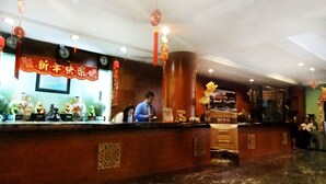 Uma área de recepção de hotel com piso de mármore, balcão de atendimento e objetos decorativos, incluindo um relógio e uma placa.