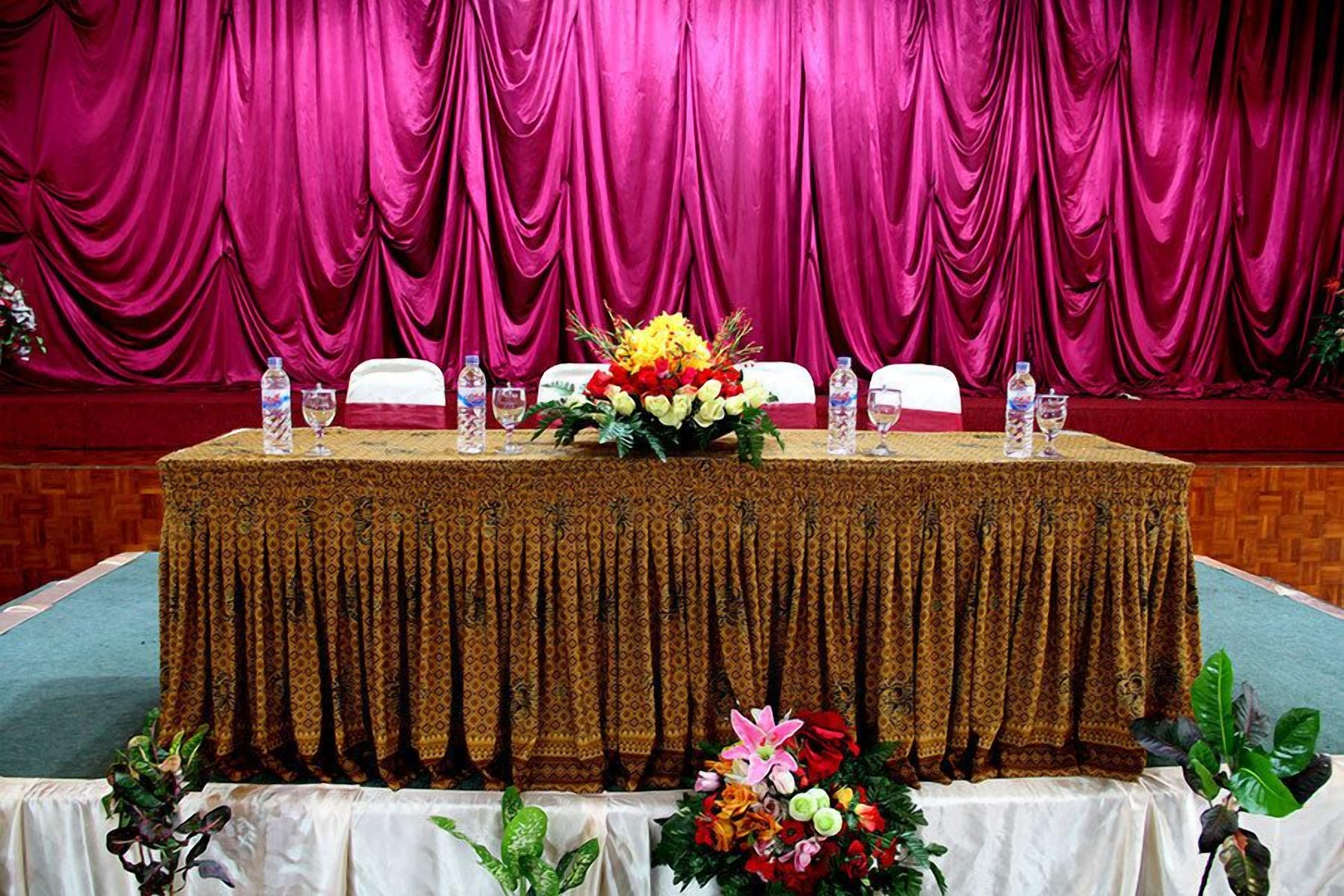 Ein Konferenztisch mit gemustertem Tischläufer, Wasserflaschen und floralen Tischdekorationen.