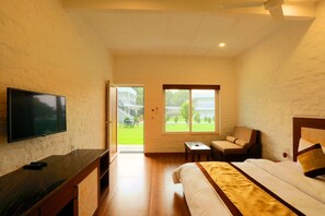 Relax in a spacious room with a large bed, flat-screen TV, and a small table with a chair, offering a view of the outdoors.