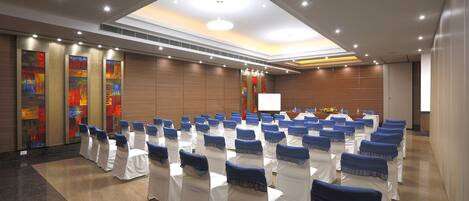 A conference room with rows of white chairs, blue headrests, and a large screen at the front.