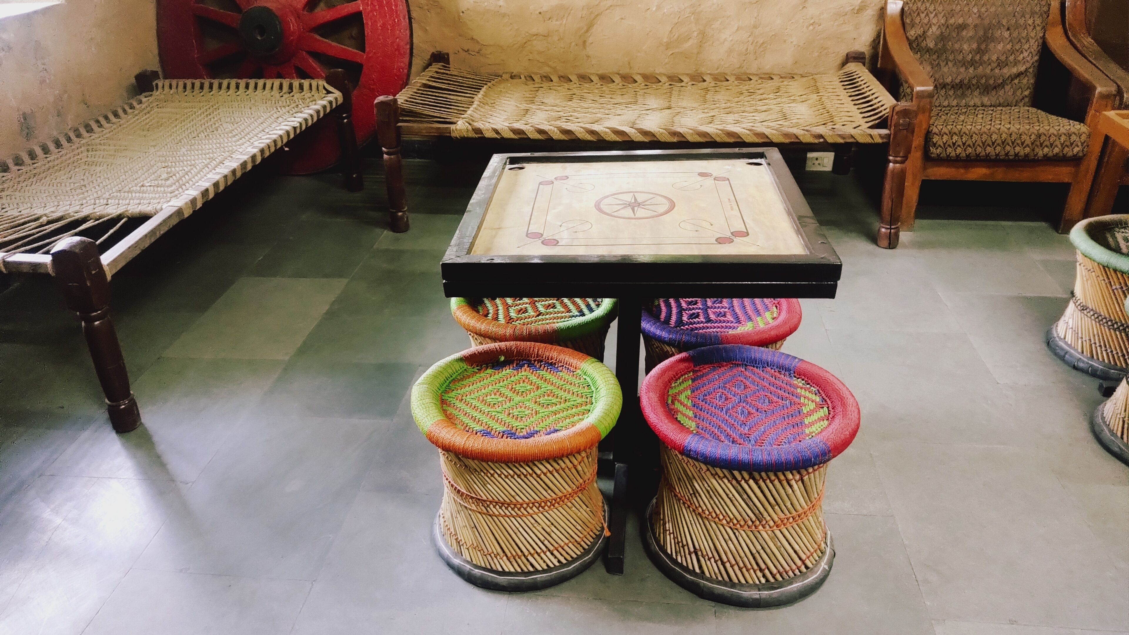 Une pièce au décor traditionnel, avec une table en osier, quatre tabourets colorés en osier et un banc en bois.
