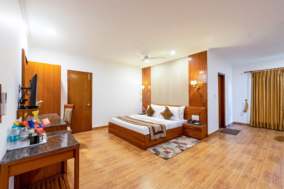 Una habitación de hotel con cama, escritorio, silla y una mesita con objetos encima.
