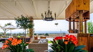 A covered outdoor seating area with wicker furniture, potted plants, and a view of the landscape. - Mooiplaas Guesthouse (Oudtshoorn)