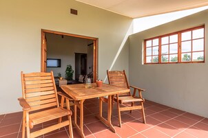 A wooden table and chairs on a tiled patio with a view of the outdoors.