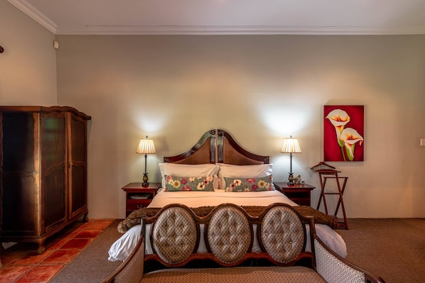 Une chambre à coucher avec un lit en bois, deux tables de chevet avec des lampes, une armoire en bois et un tableau floral accroché au mur.