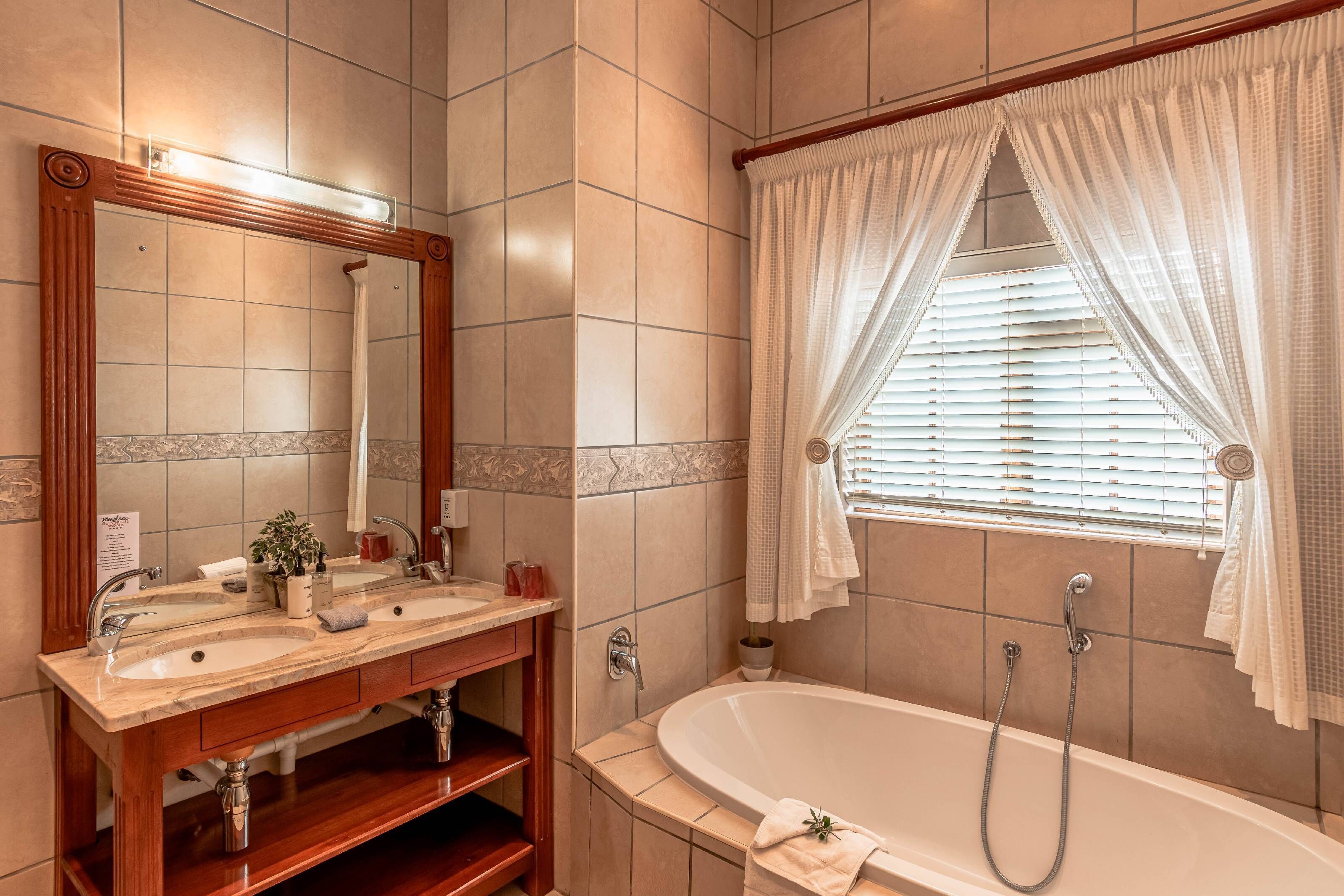 A bathroom with two sinks, a large mirror, a bathtub, and a window with curtains.