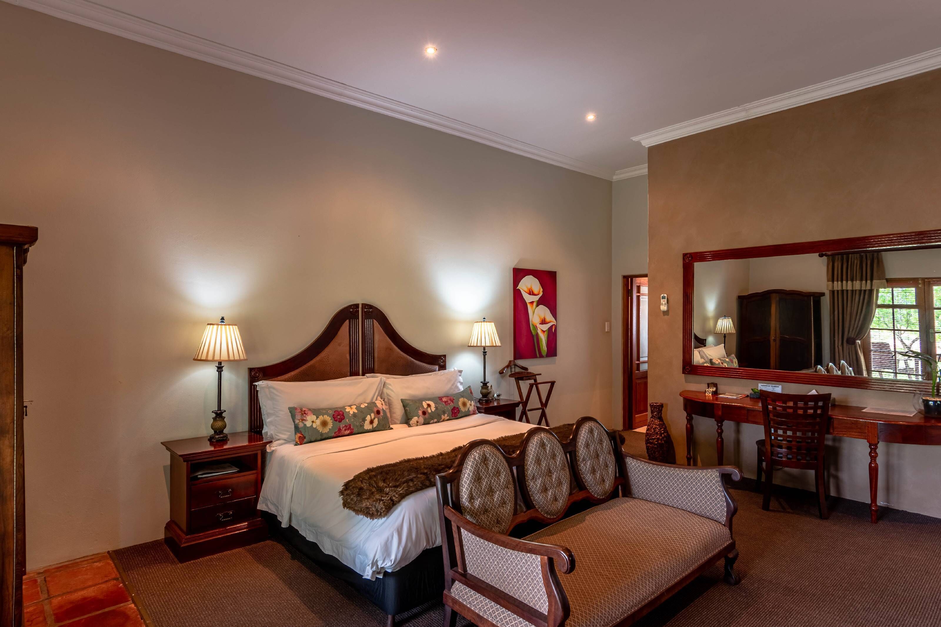 Une chambre d’hôtel avec un lit, des lampes de chevet, un bureau avec une chaise, un miroir et un tableau au mur.