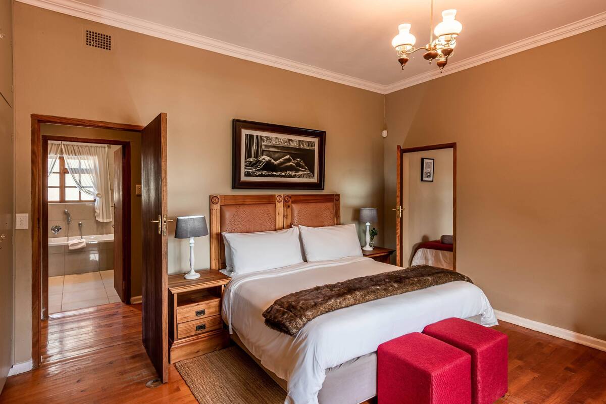 Ein Schlafzimmer mit einem hölzernen Kopfteil, einem großen Bett mit weißer Bettwäsche, einer roten Bank, einem Nachttisch mit Lampe und einem gerahmten Bild an der Wand.