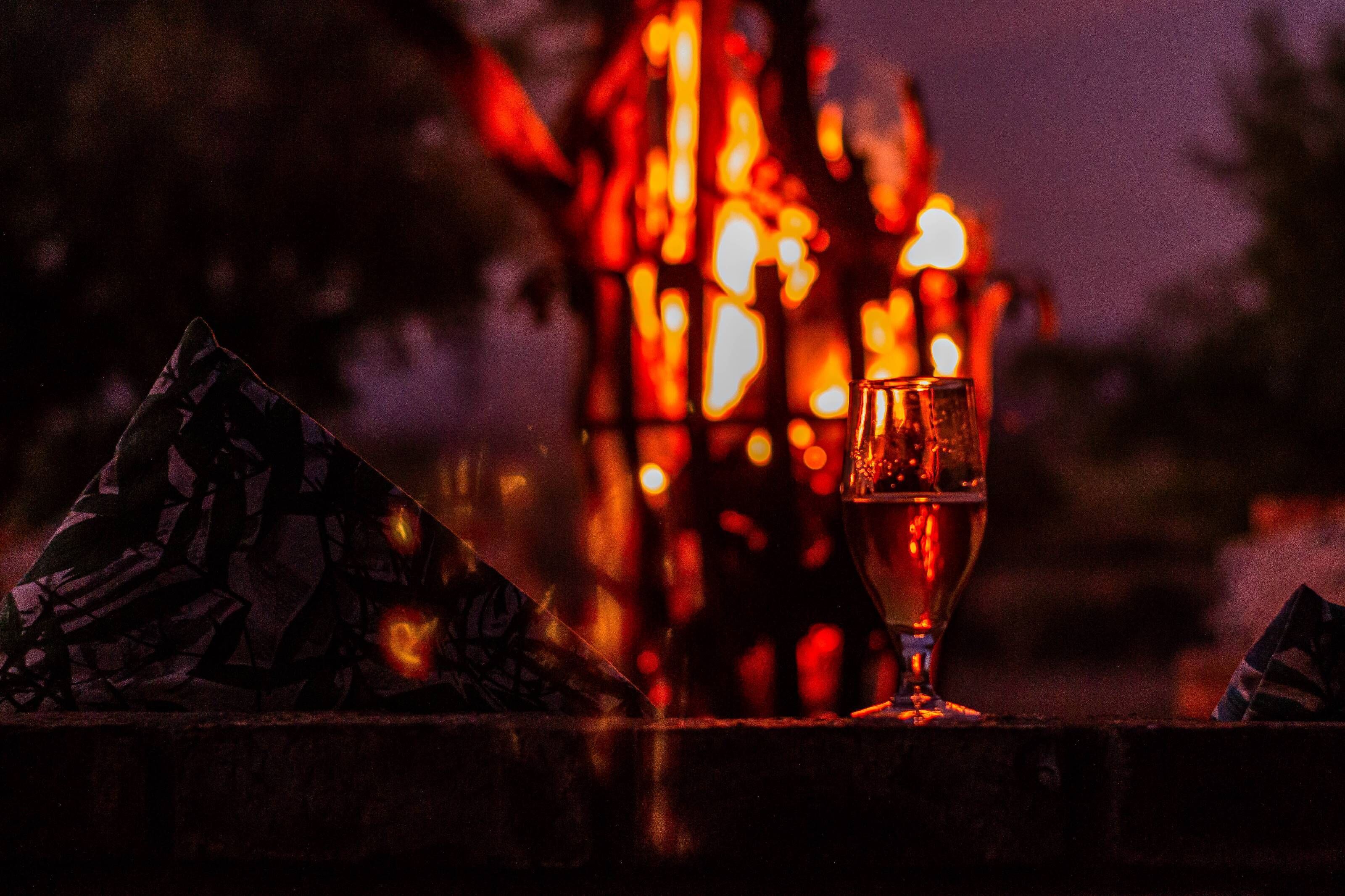 A glass of wine on a table with a patterned napkin, set against a backdrop of blurred lights.