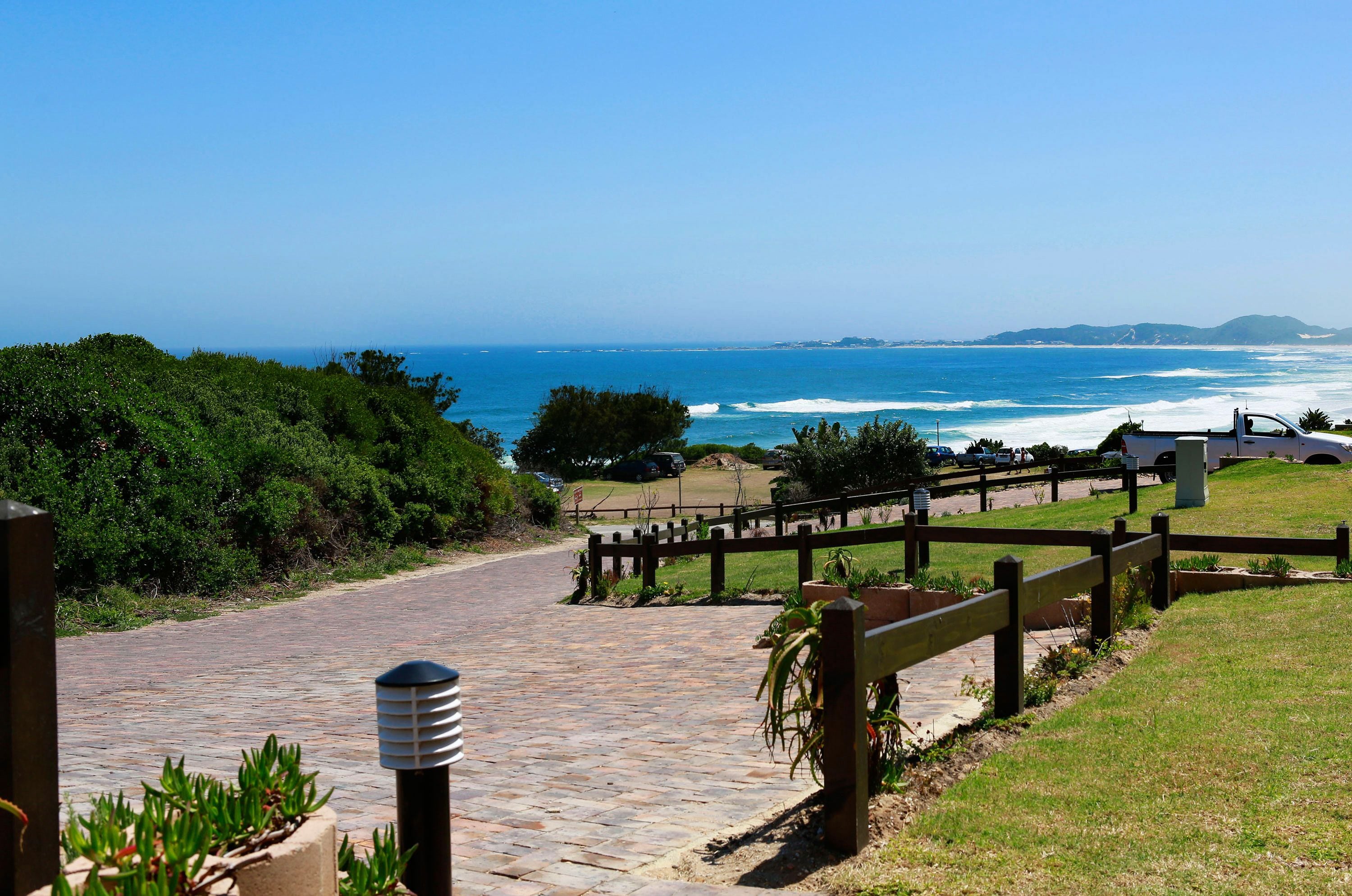 A paved pathway leading to a beach with a wooden fence and potted plants.
