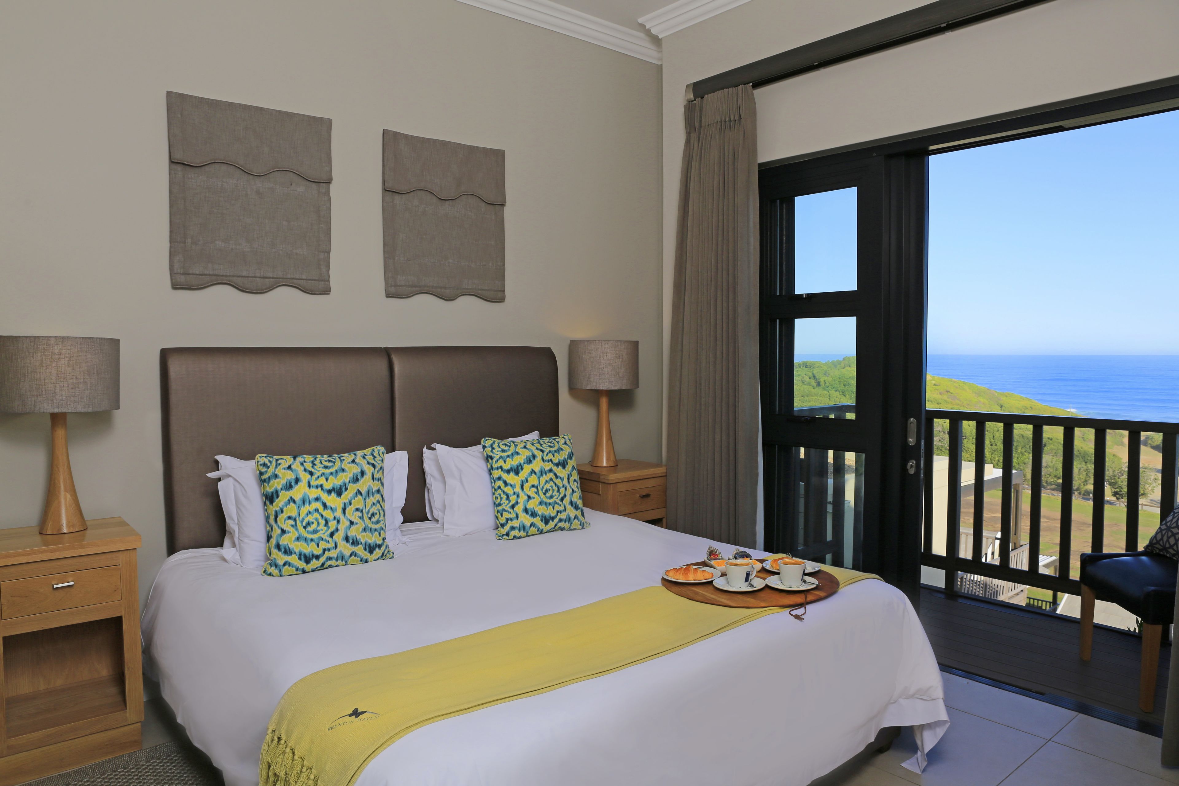 A hotel room with a bed, two nightstands, a balcony with a view of the sea, and a chair.