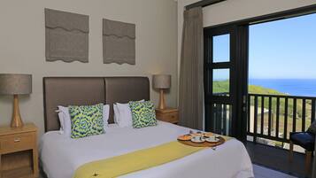 A hotel room with a bed, two nightstands, a balcony with a view of the sea, and a chair.