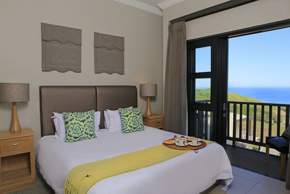 A hotel room with a bed, two nightstands, a balcony with a view of the sea, and a chair. - Brenton Haven Beachfront Resort (Knysna)