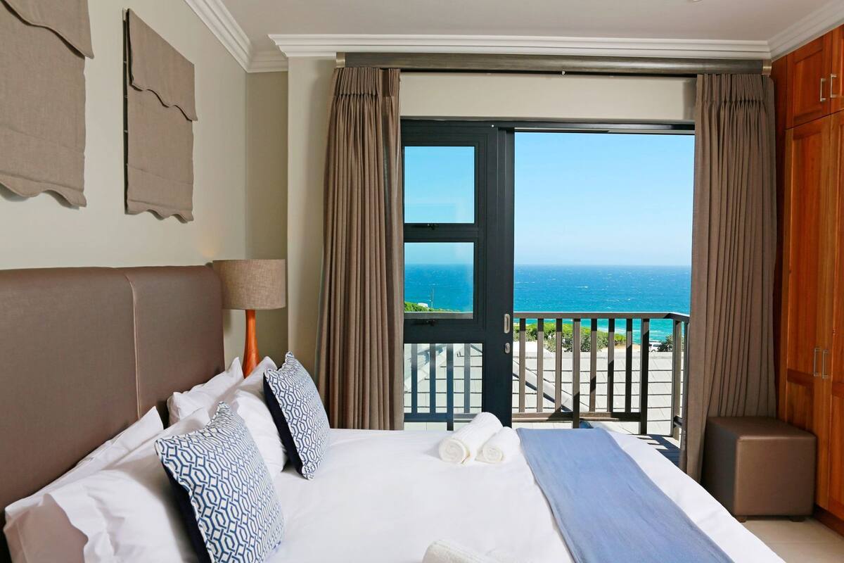 Een hotelkamer met een bed, nachtkastje, lamp, uitzicht op zee en een balkon.