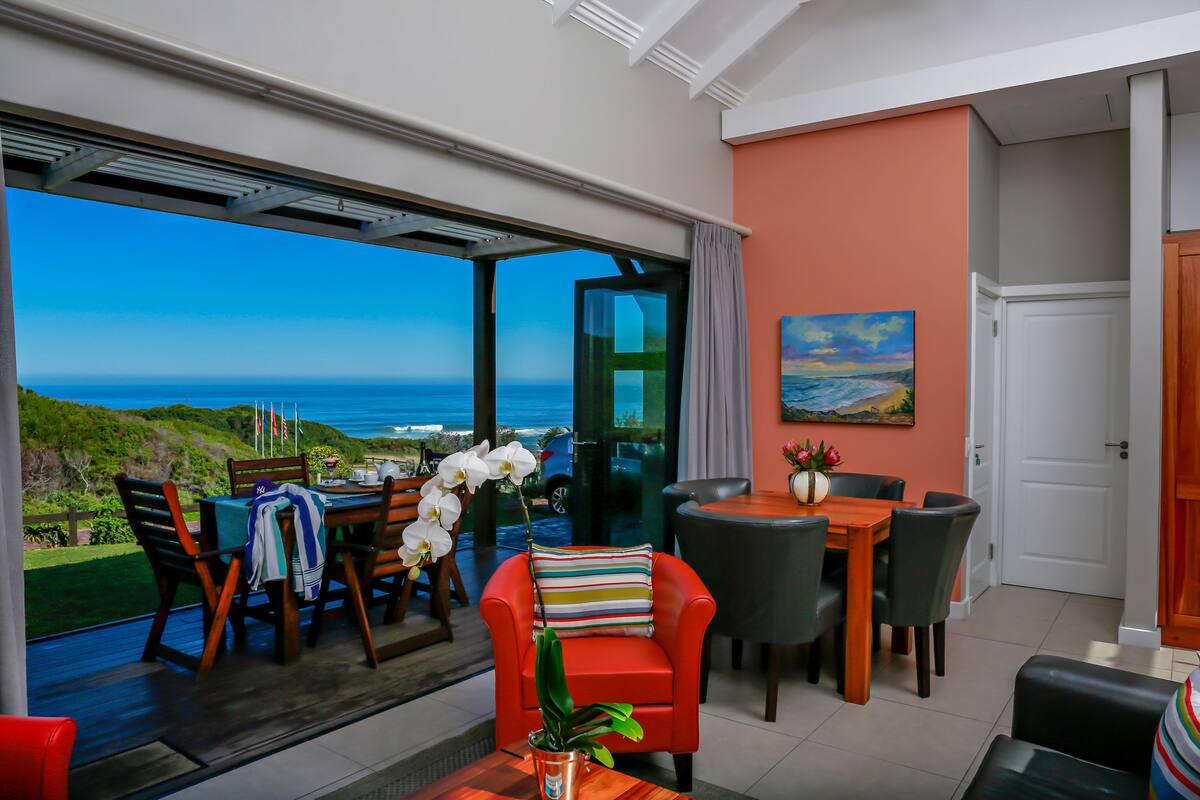 Een ruime kamer met een grote schuifglazen deur die uitkomt op een balkon met uitzicht op zee.