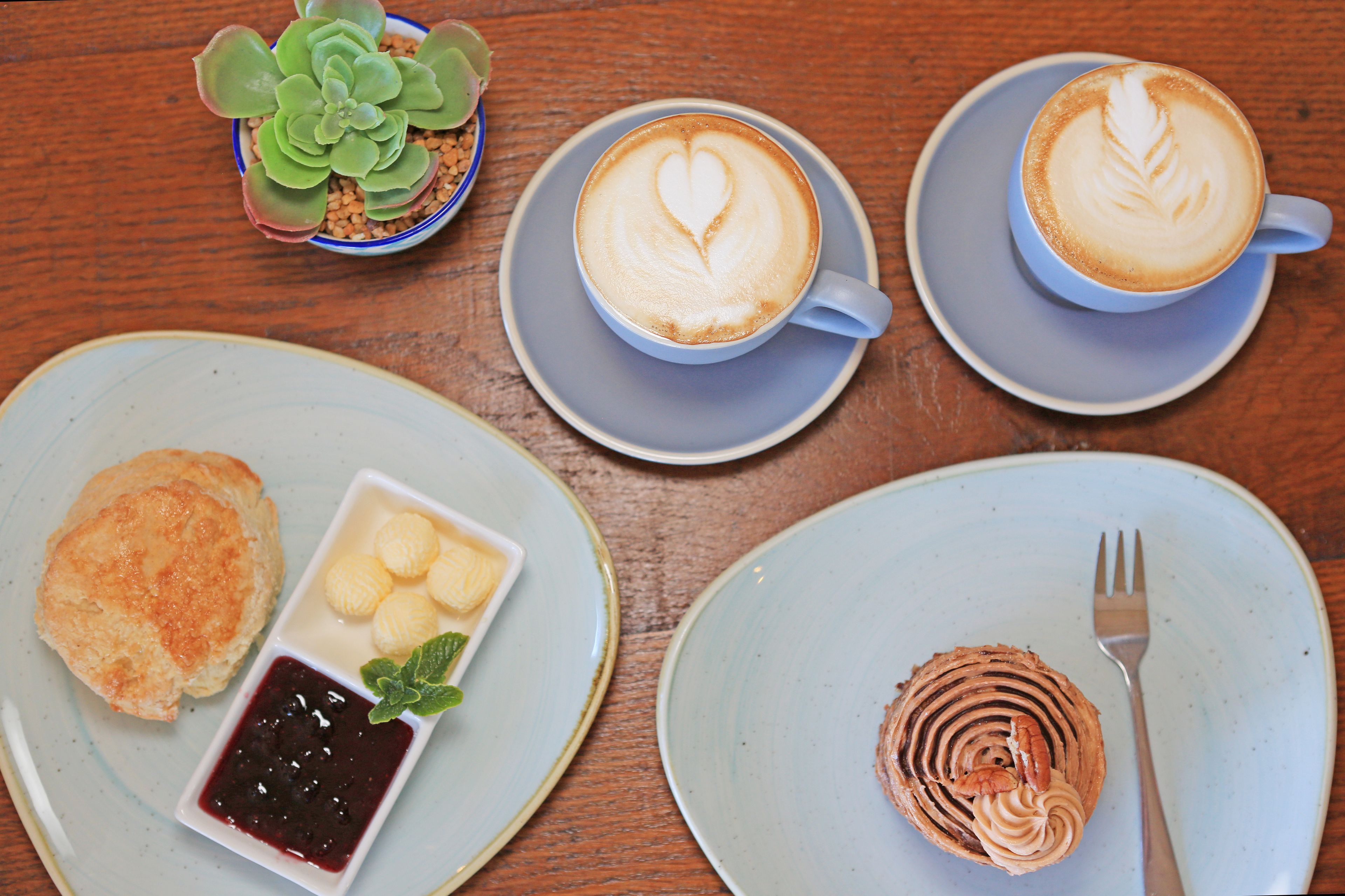 A table with a cup of coffee, a biscuit with jam, a small plant, and a plate with a pastry.
